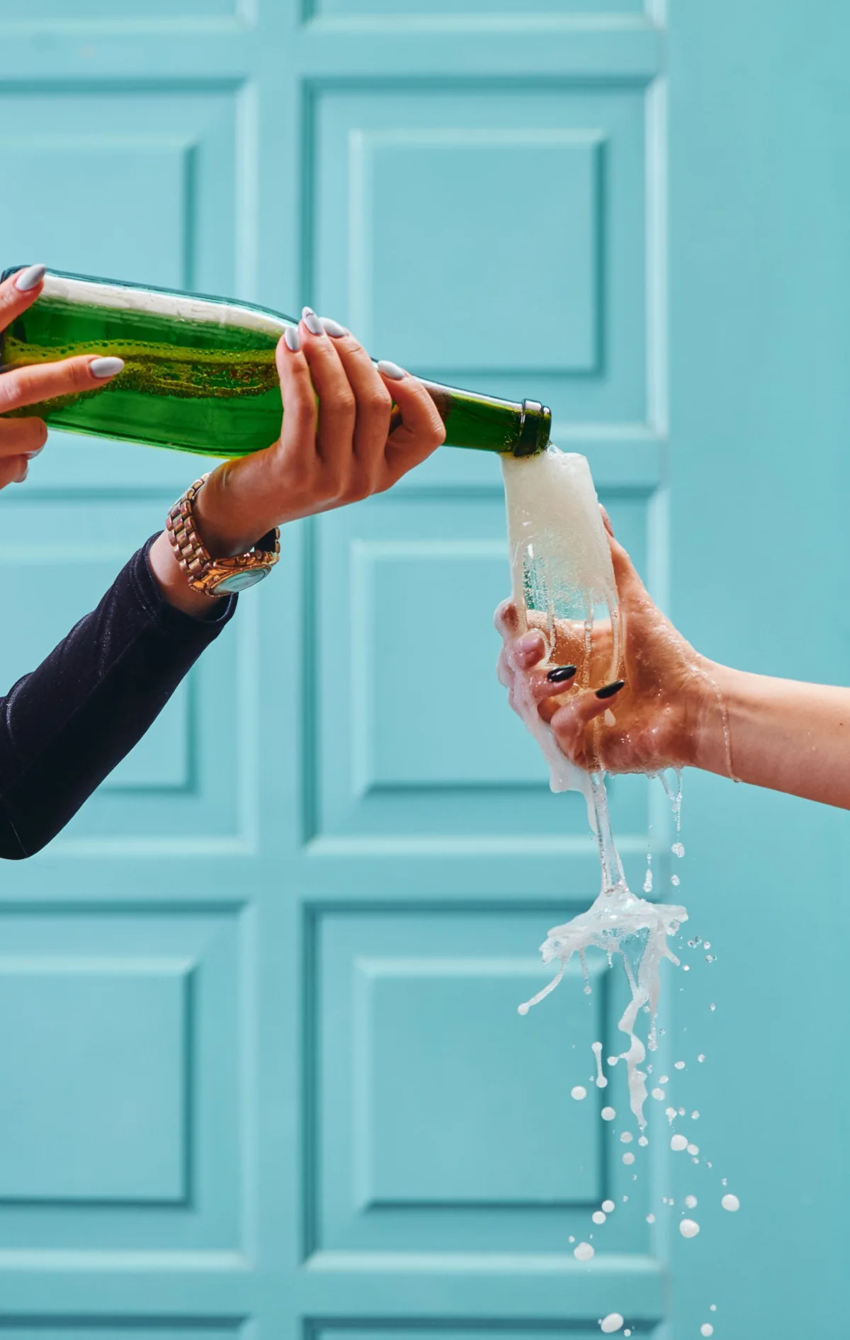 Champagne overflowing a flute against a turquoise doorway