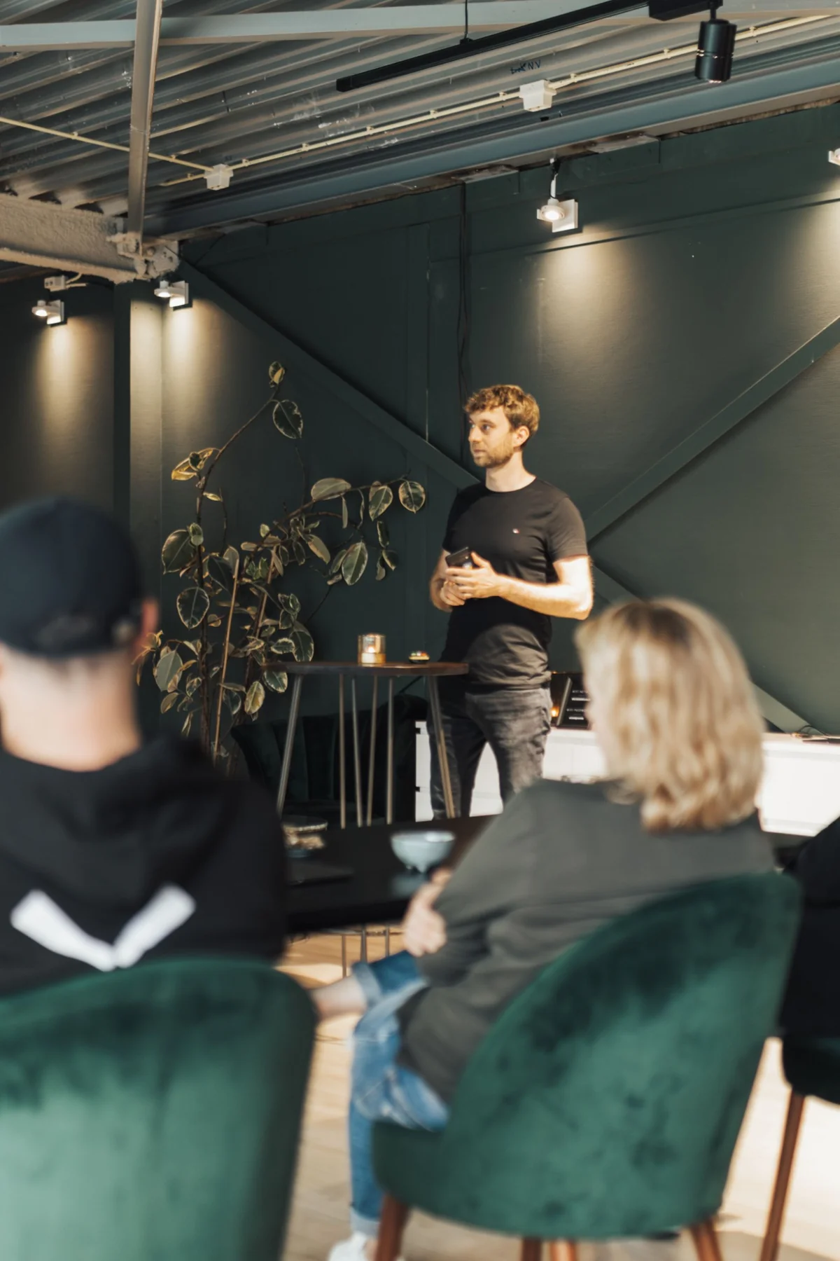 A facilitator standing in front of seated workshop attendees in a room with green walls.