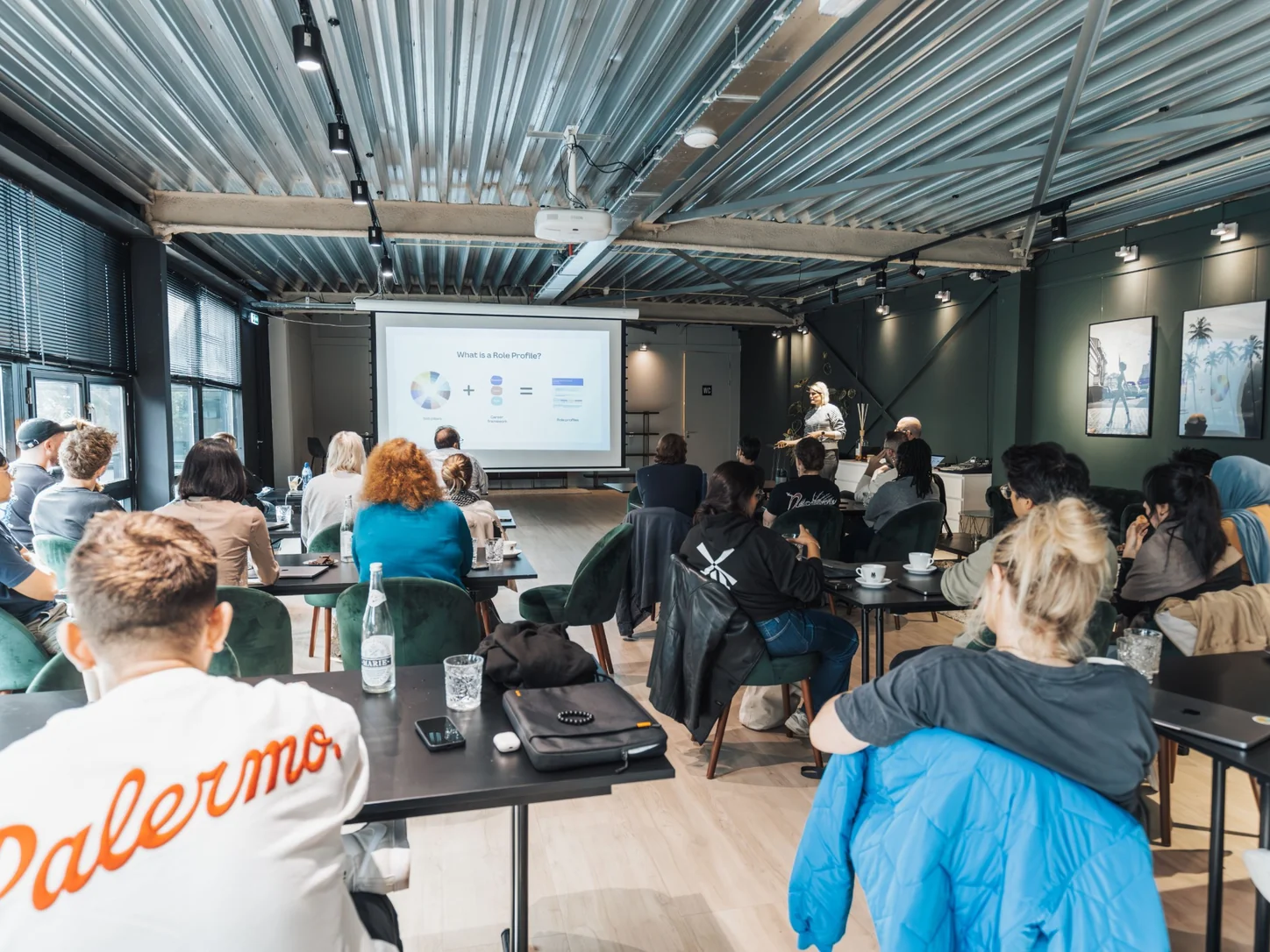 Attendees seated at tables facing a facilitator and presentation screen during a business workshop.